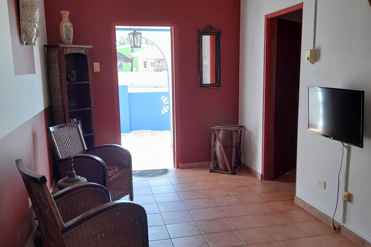 A room with a ceiling fan, a television, wicker furniture, and a tiled floor.