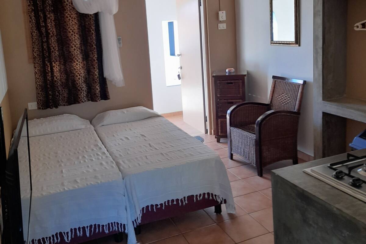 A bedroom with a bed, a ceiling fan, a wardrobe, and a small table with a gas stove.