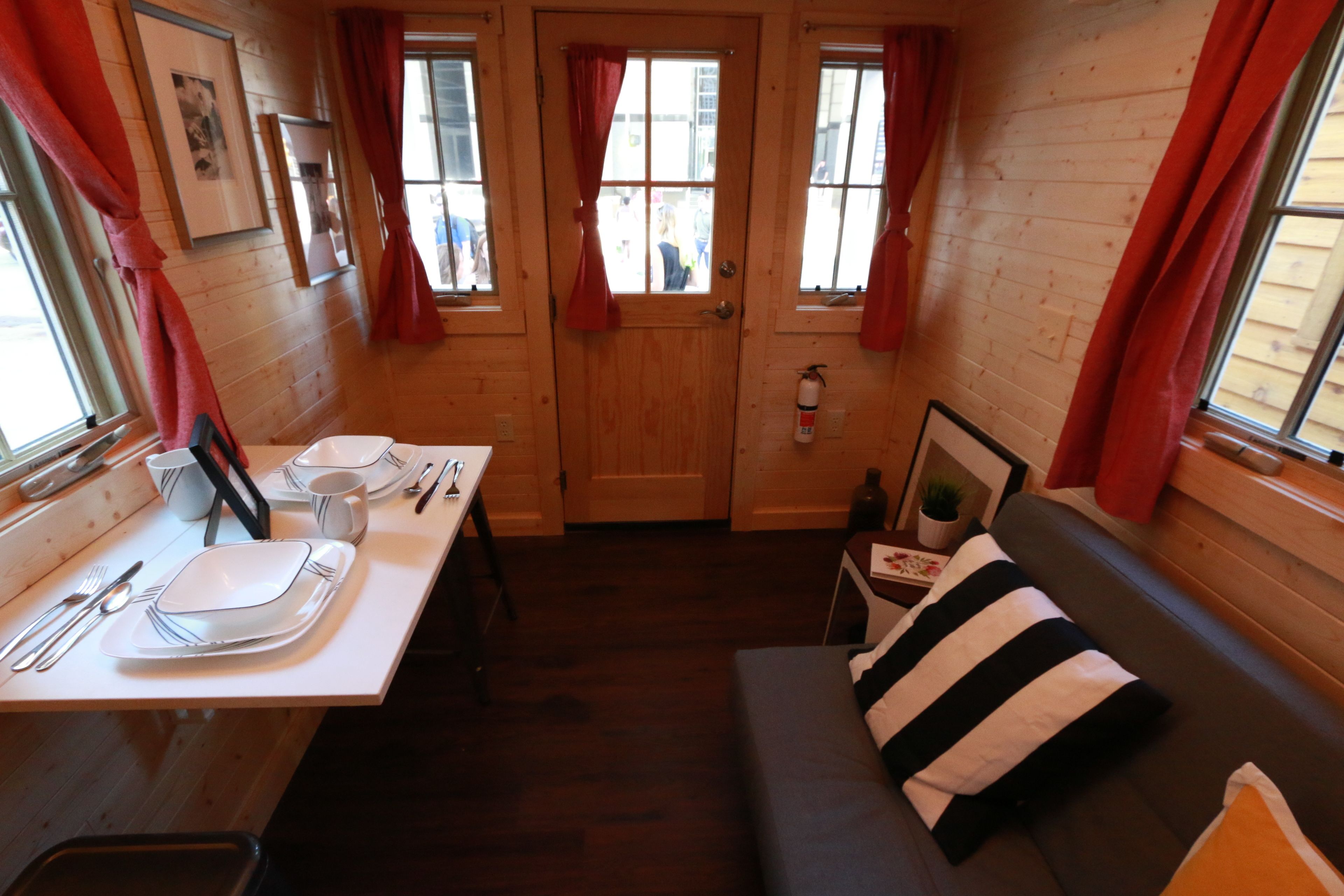 Une pièce chaleureuse avec une porte en bois, une table à manger dressée avec des assiettes, des couverts et une tasse, un canapé avec des coussins à rayures et une petite table sur laquelle est posée une plante en pot.
