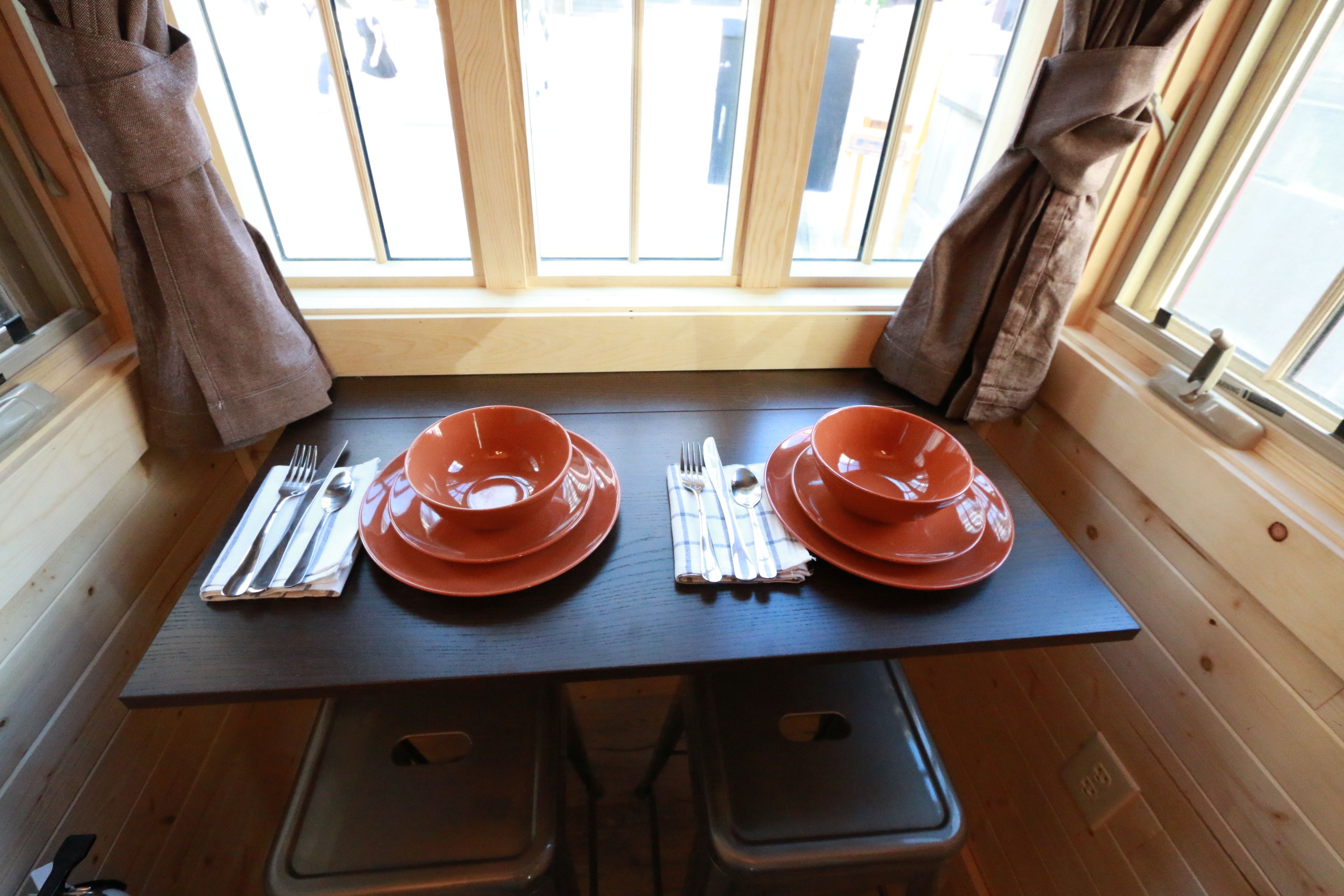 A dining table with two orange plates, cutlery, and a napkin.