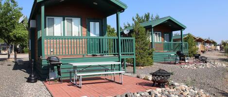 Two cabins with green roofs and wooden exteriors, each with a balcony and outdoor seating area.