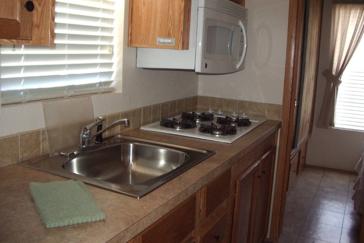 Una cocina compacta con un lavamanos de acero inoxidable, un microondas y una estufa a gas.