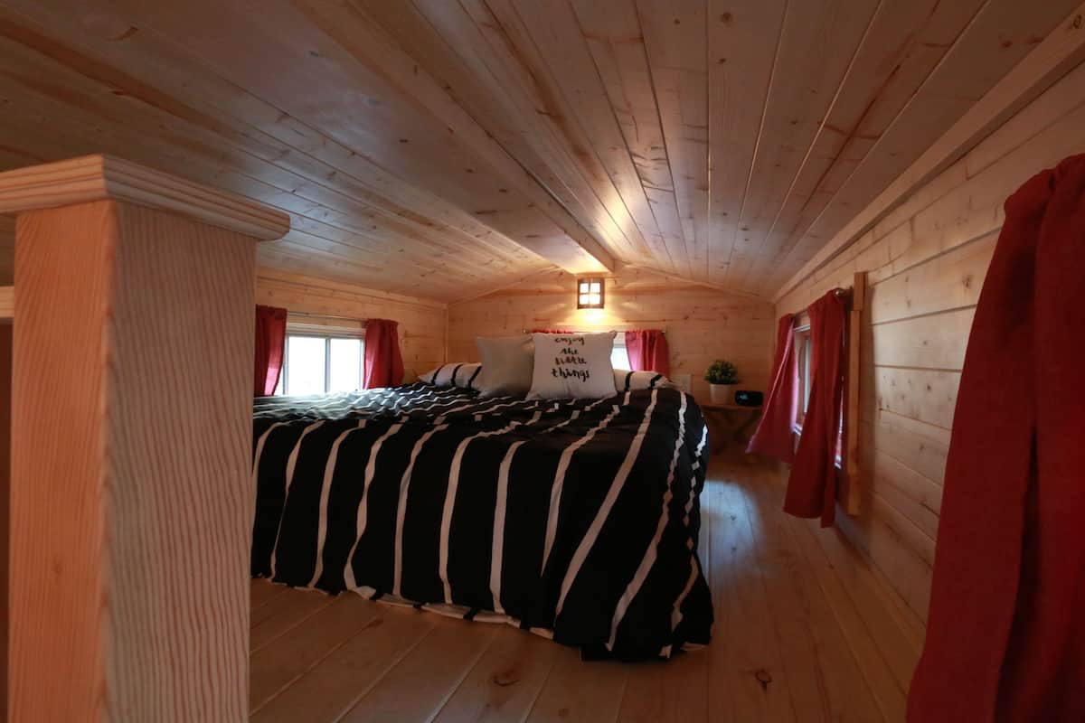 Un dormitorio acogedor de estilo cabaña, con cama, mesita de noche y ventana con cortinas.