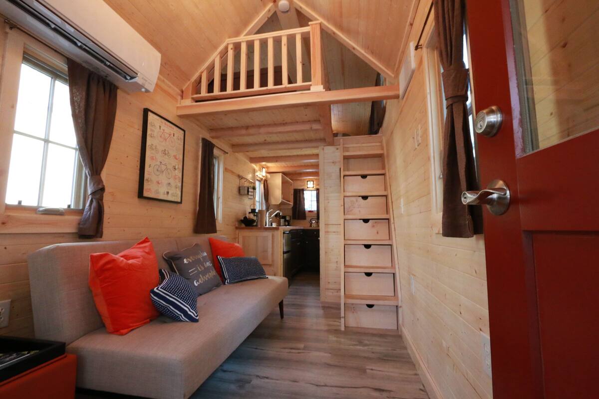 Un interior de cabaña acogedor con una escalera de madera, un sofá con cojines y una zona de cocina.