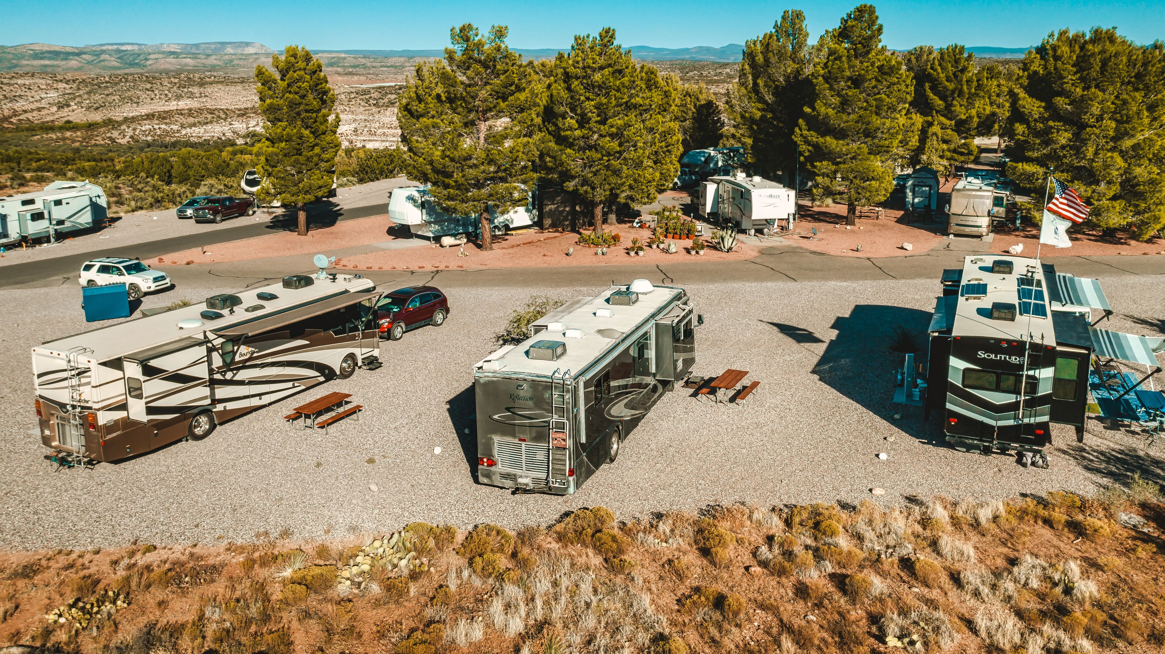 Un terrain de camping équipé d’emplacements pour camping-cars et caravanes, de tables de pique-nique et offrant une vue dégagée sur le paysage environnant.