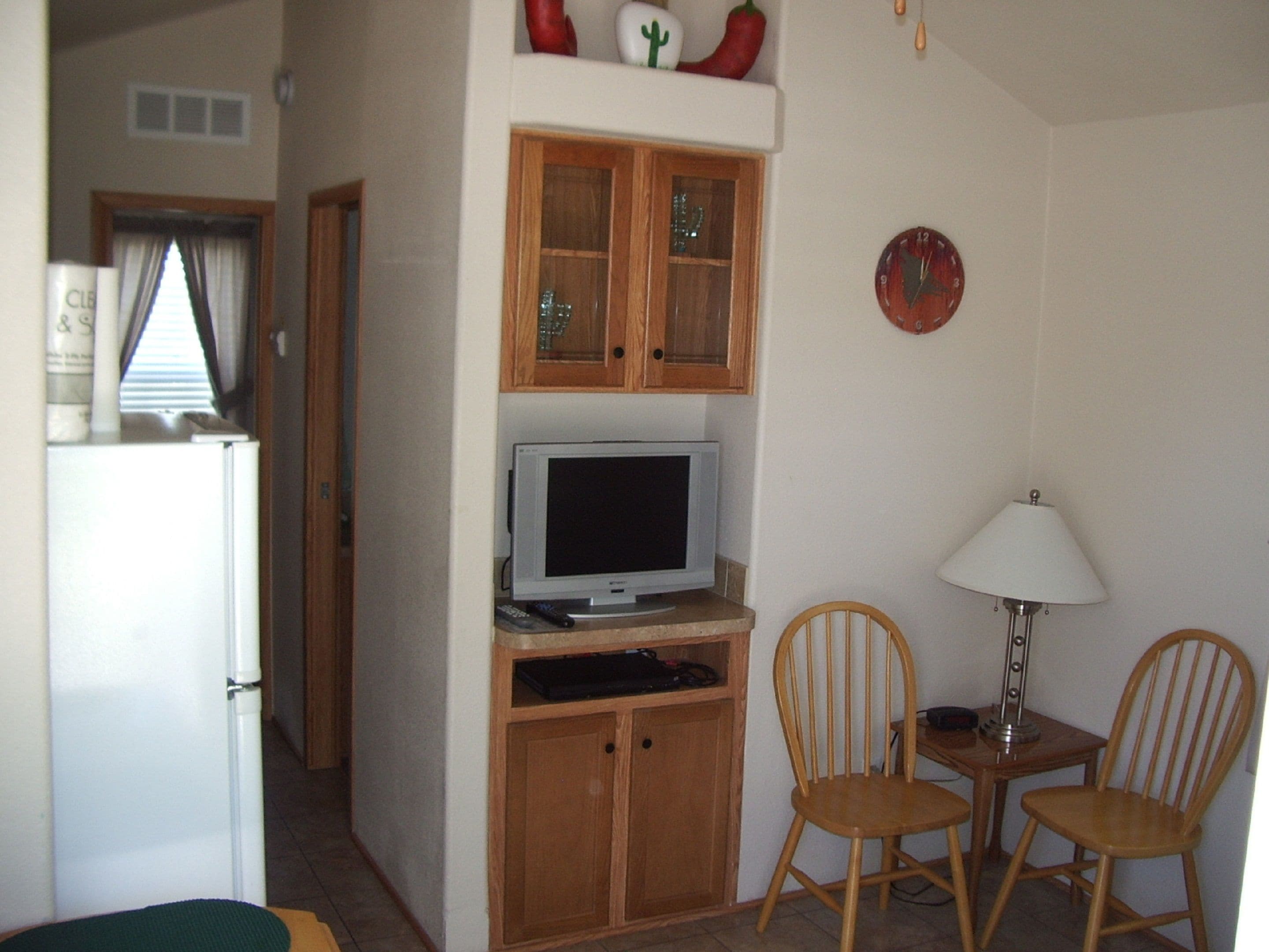 A compact living space with a kitchenette, a television, wooden cabinets, and two chairs.