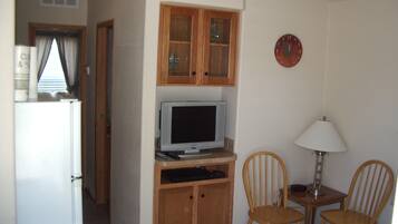 A compact living space with a kitchenette, a television, wooden cabinets, and two chairs.