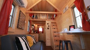L’intérieur chaleureux d’un chalet, avec un revêtement mural en bois, un canapé agrémenté de coussins à rayures, un coin cuisine et un escalier menant à une mezzanine.