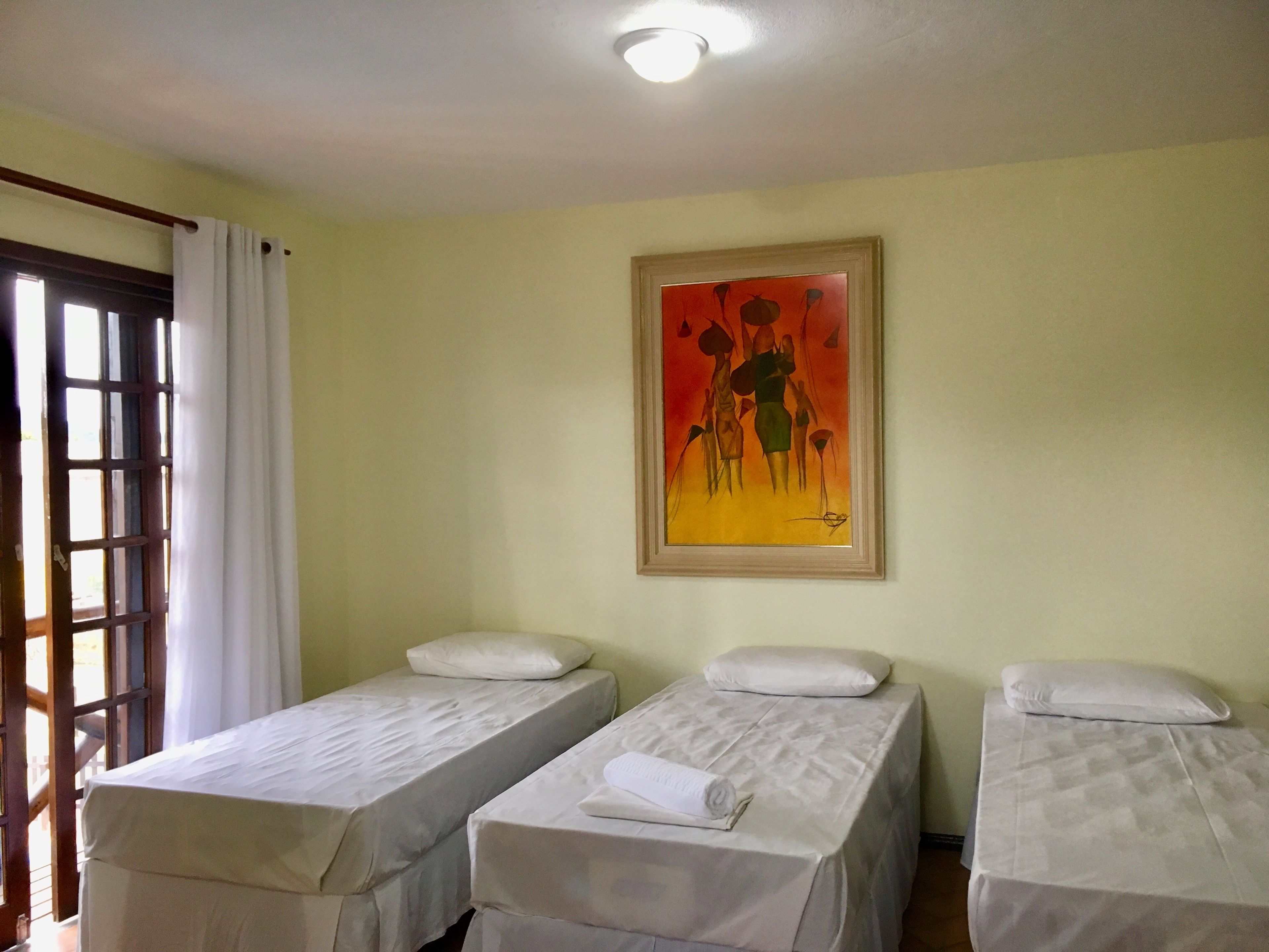A room with two single beds, a painting on the wall, and a window with curtains.