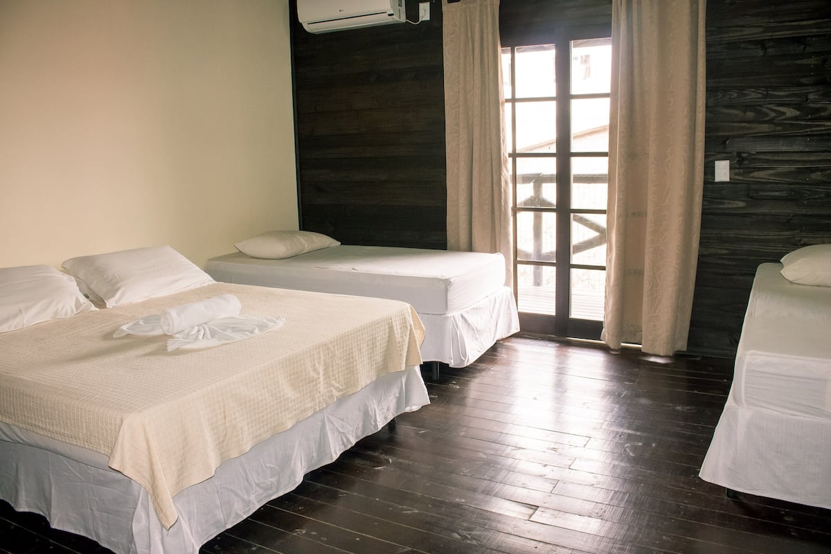 A room with two beds, wooden flooring, and a window with curtains.