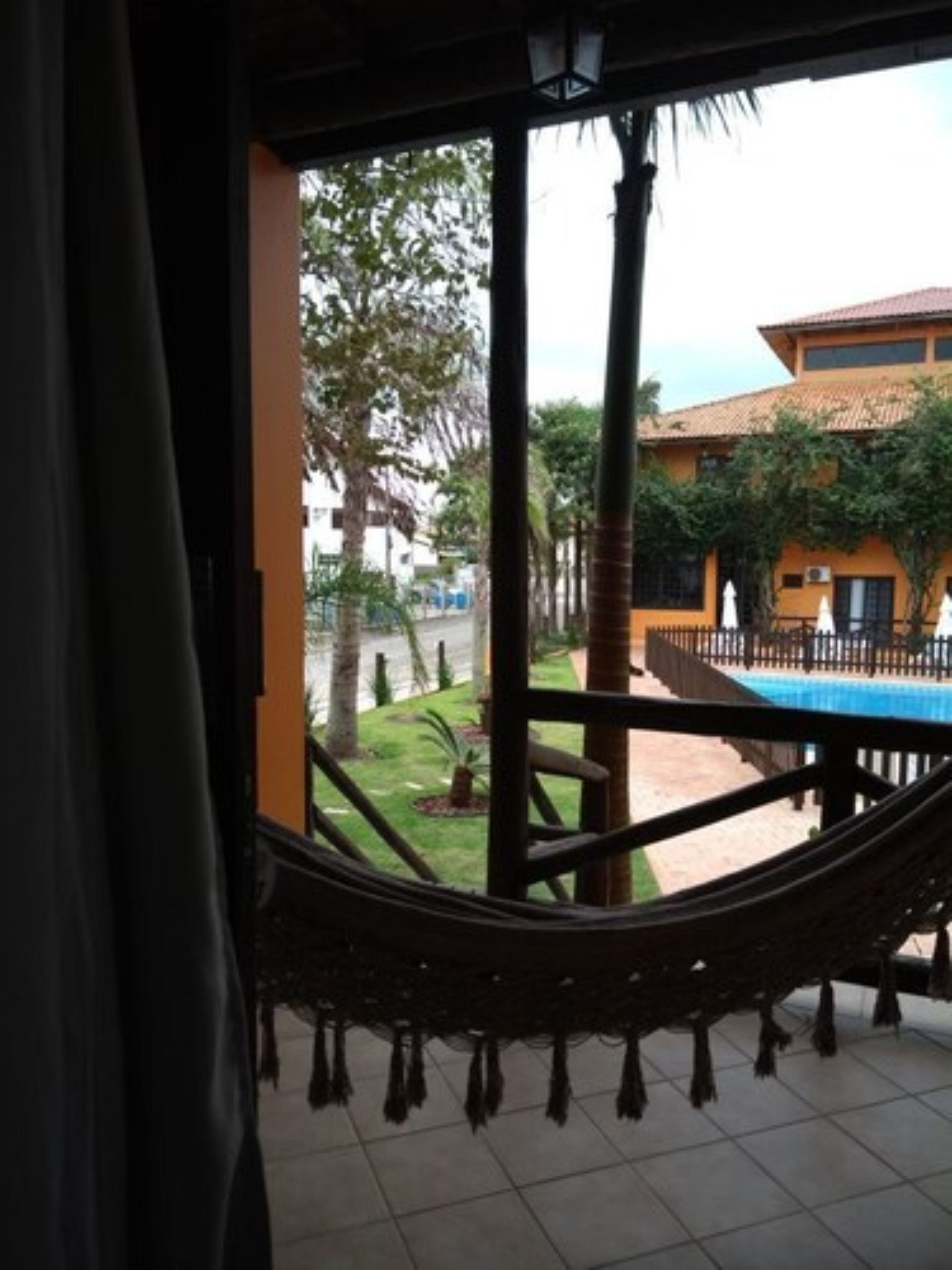 Eine Hängematte auf einem Balkon mit Blick auf einen Pool und ein Gebäude mit einem Ziegeldach.