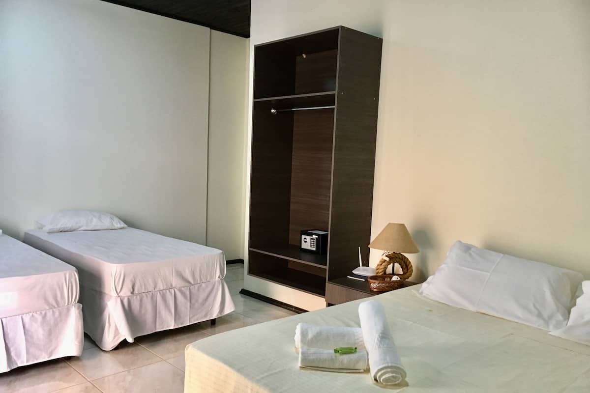 A hotel room with two single beds, a large wardrobe, a bedside table with a lamp, and a rolled towel on the bed.