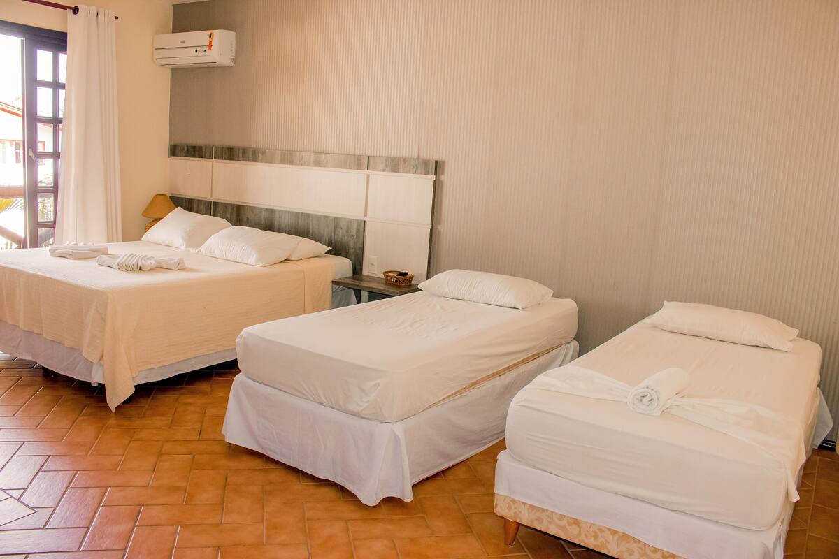 A hotel room with two beds, a headboard, a nightstand, and a window with curtains.