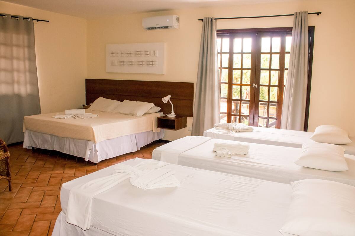A hotel room with two beds, a wooden headboard, a nightstand, a lamp, and a window with curtains.