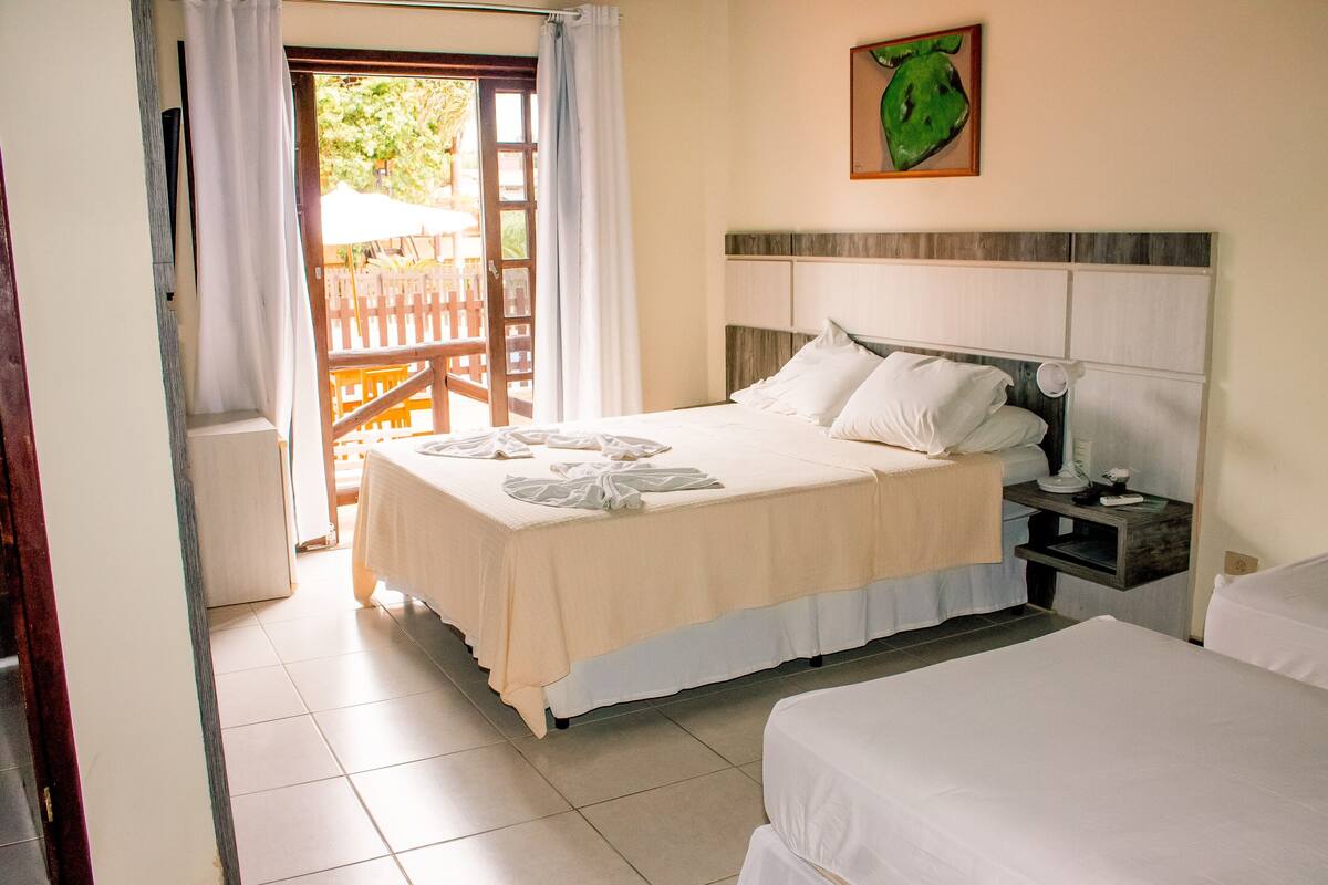 A hotel room with a bed, a bedside table, and a view of the outside.