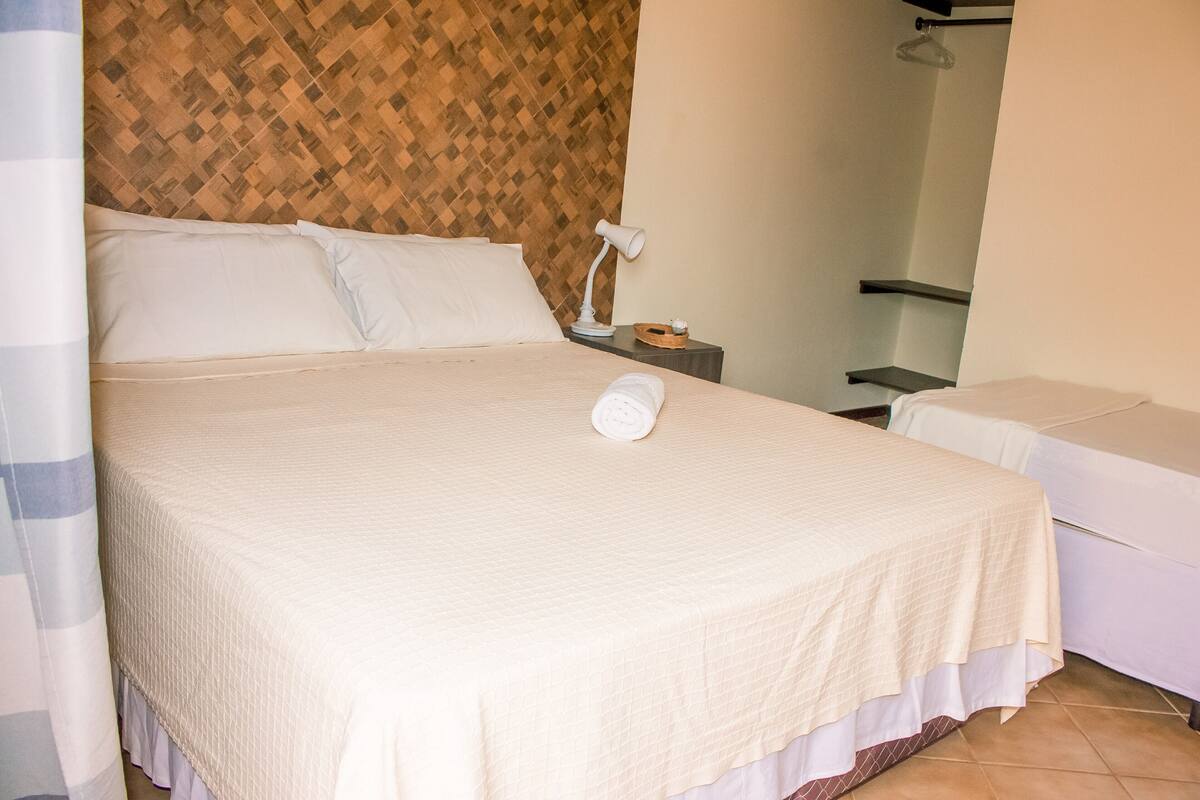 A neatly made bed with a white duvet, a bedside lamp, and a small wooden nightstand with a cup and saucer.