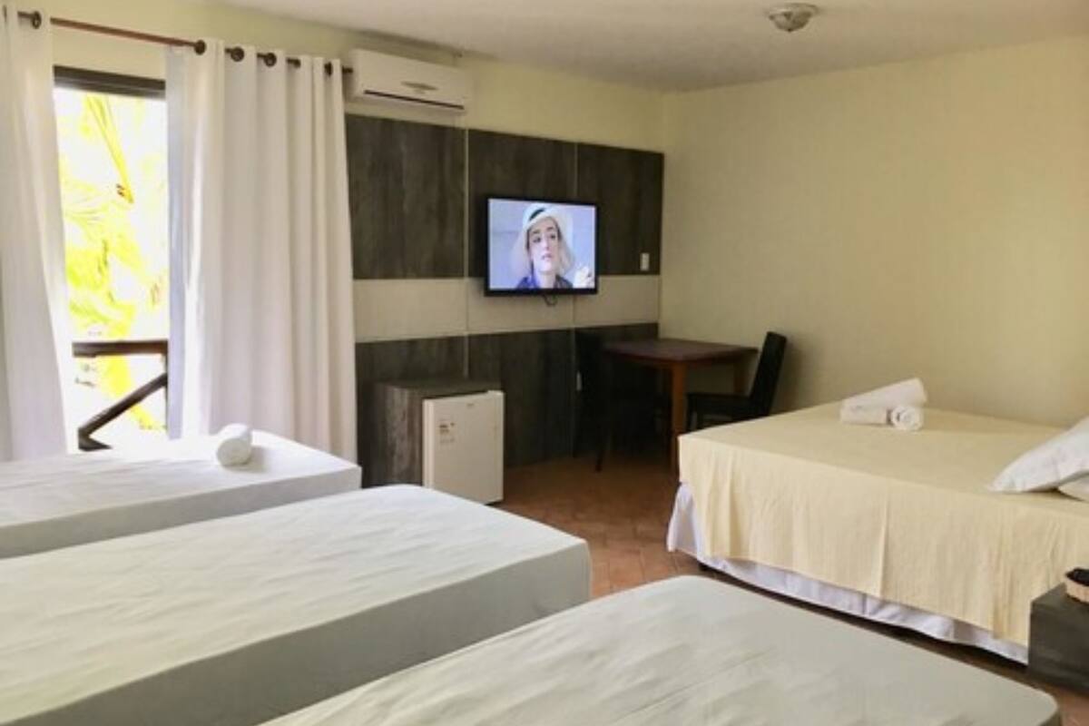 A hotel room with two beds, a desk, a television, and an air conditioning unit.