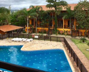 A swimming pool with lounge chairs, a fenced area, and a building with a tiled roof. - Pousada Canto Grande (Bombinhas)