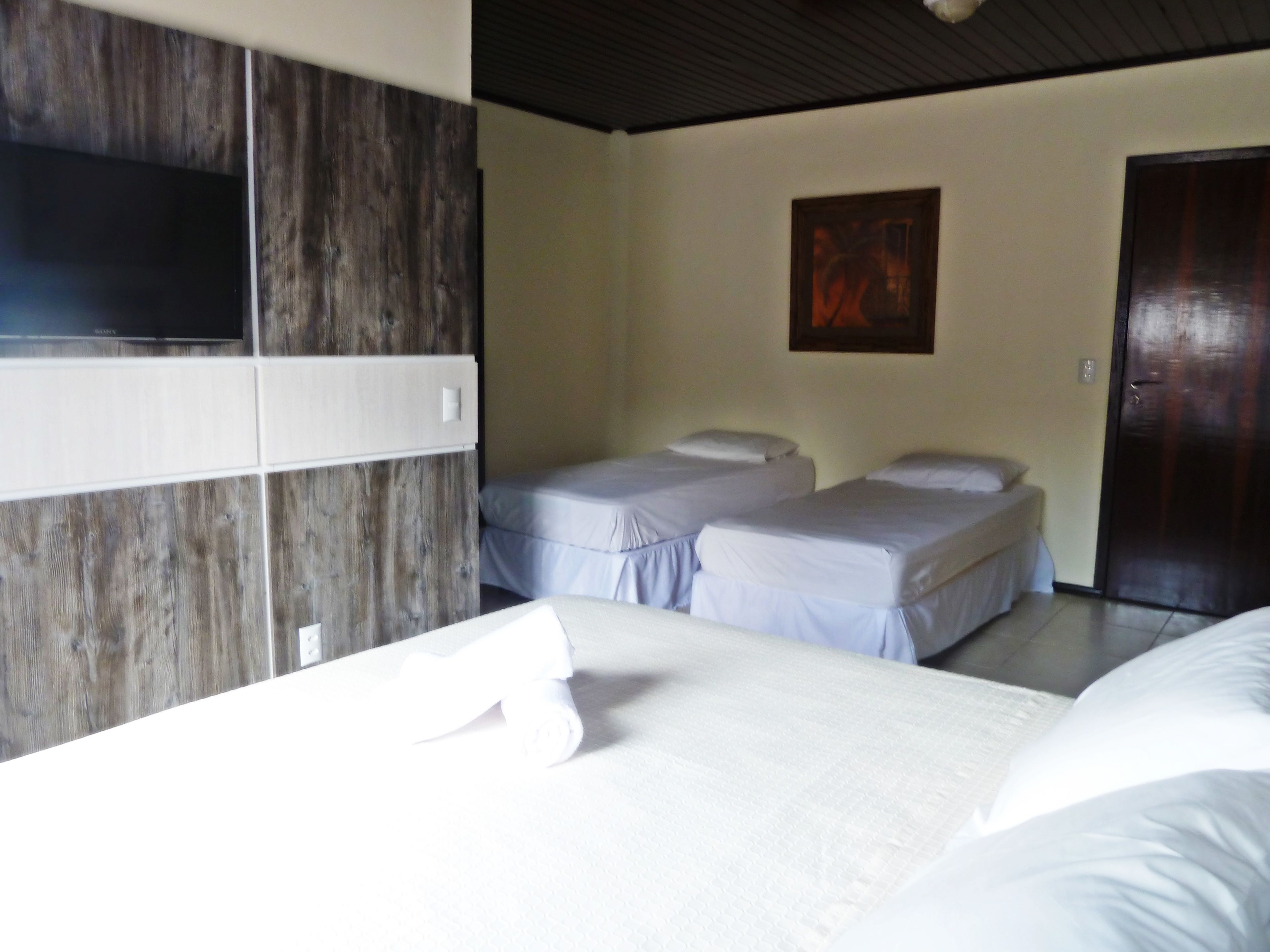 A hotel room with two single beds, a wooden panel wall, a painting, and a door.