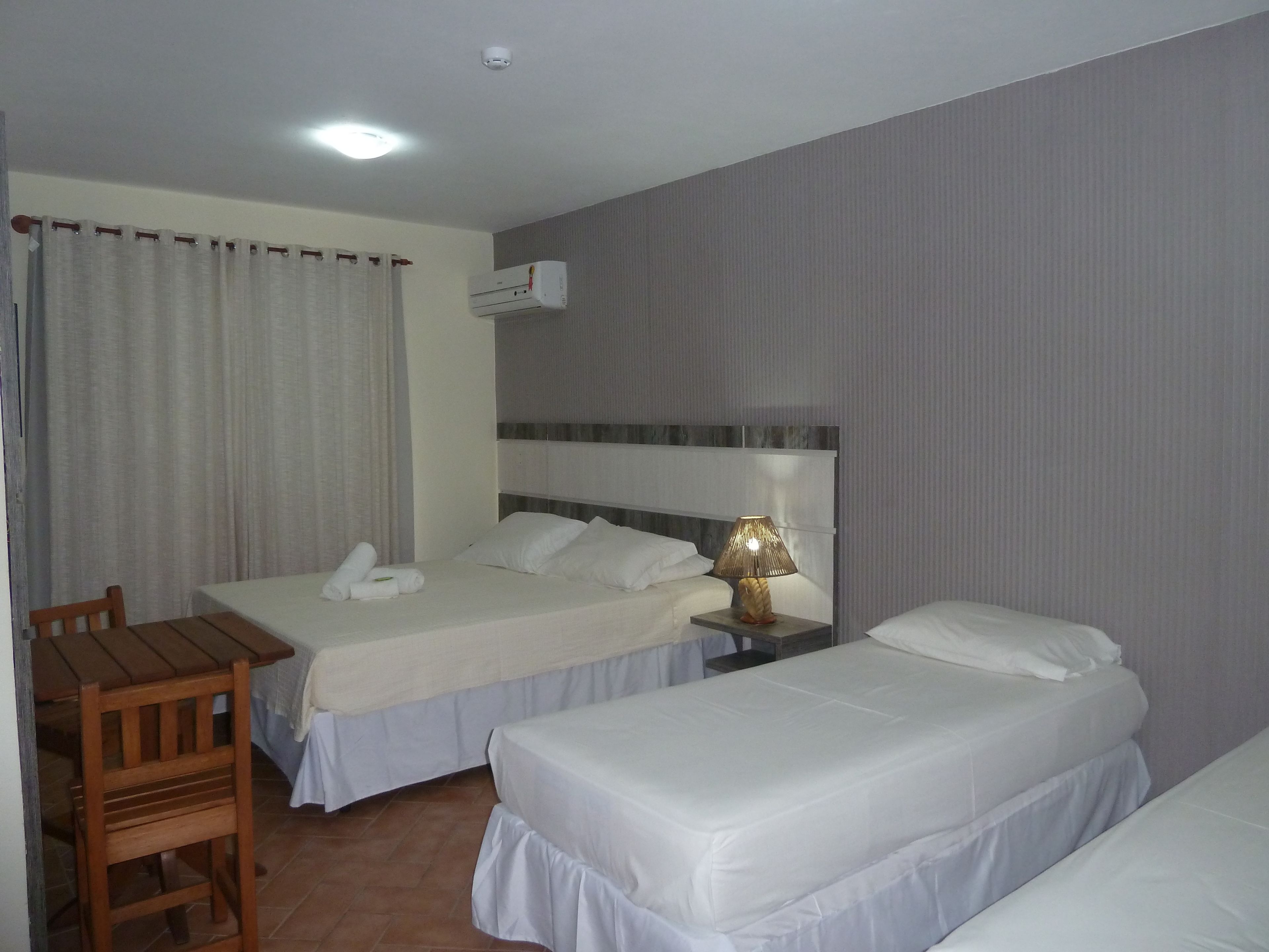 Una habitación de hotel con dos camas, un escritorio, una silla y una mesita de noche con lámpara.