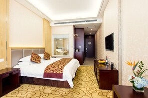 Habitación de hotel con una cama grande, un escritorio, un espejo, un televisor y un baño visible a través de una puerta abierta.