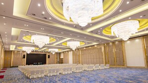 Une grande salle de conférence avec des rangées de chaises blanches, une scène et un grand lustre.