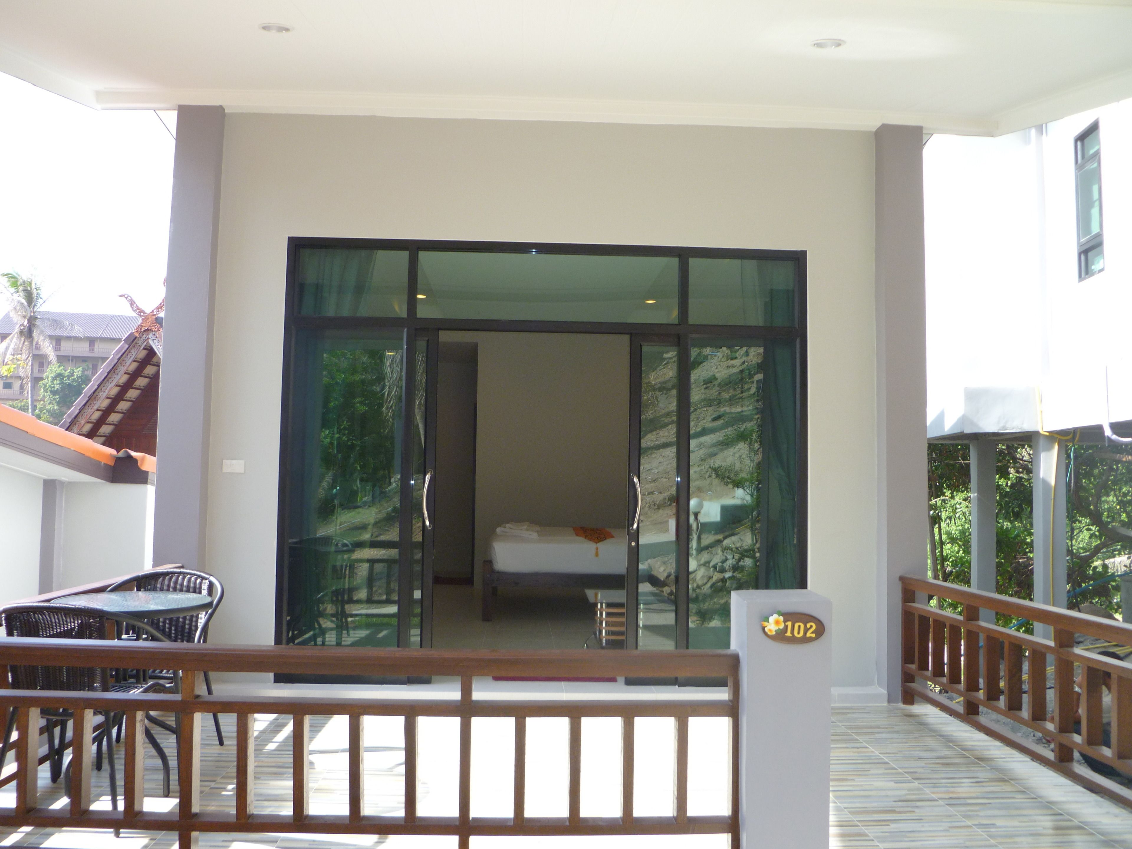 Una habitación de hotel con puerta corredera de vidrio, una cama y un balcón con baranda de madera.