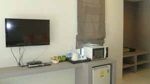A hotel room with a flat-screen TV, a microwave, a refrigerator, and a small counter with a basket and bottles. - Sun Moon Star Resort Koh Phangan (Ko Pha-ngan)