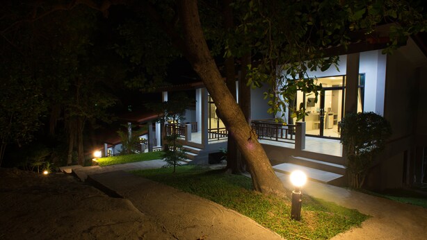 A nighttime view of a building with a well-lit entrance, a covered outdoor area, and a visible staircase leading to the entrance. - Sun Moon Star Resort Koh Phangan (Ko Pha-ngan)