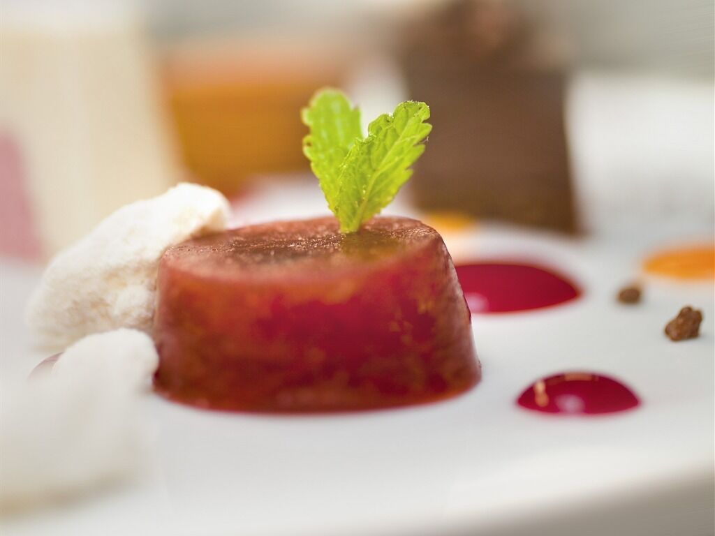 Un postre con salsa roja y una hoja de menta como adorno en un plato blanco.