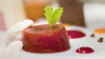 Un postre con salsa roja y una hoja de menta como adorno en un plato blanco.
