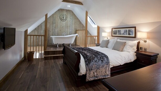 A bedroom with a large bed, a bathtub, and a wooden staircase. - The New Inn (Dorchester)