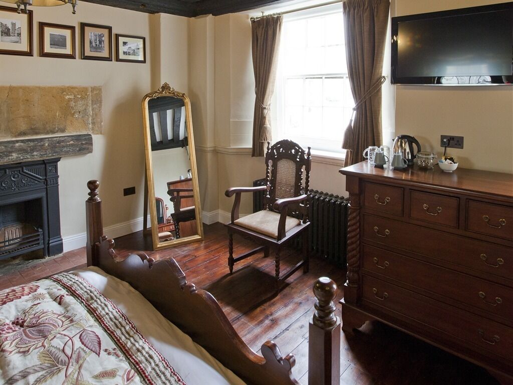 A traditional room with a bed, wooden dresser, chair, and a fireplace.