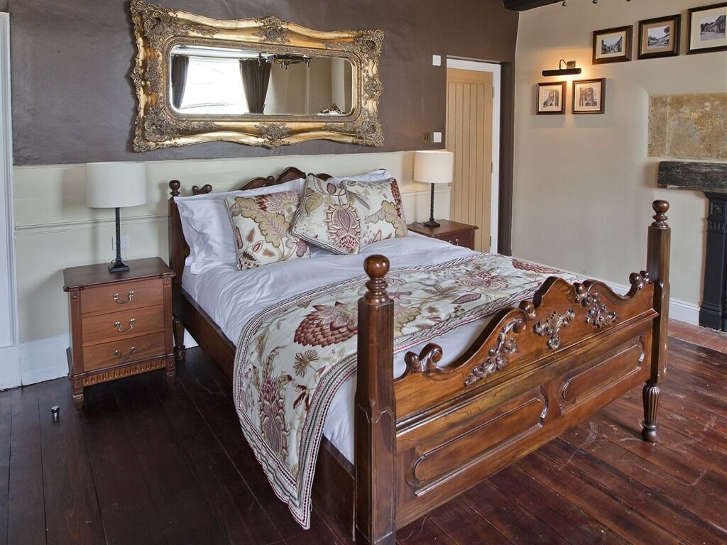 A bedroom with a large ornate bed, a wooden nightstand, a dresser, a mirror, and framed pictures on the wall.