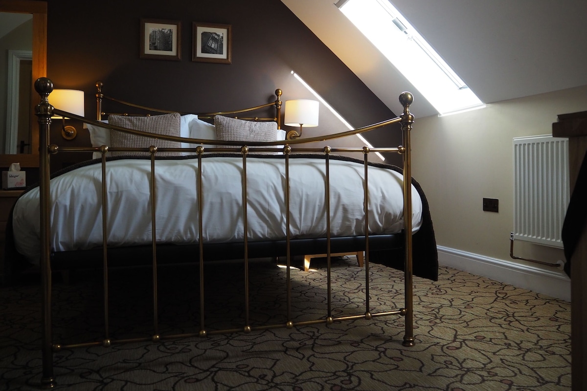 A bedroom with a bed, a skylight, a radiator, and framed pictures on the wall.