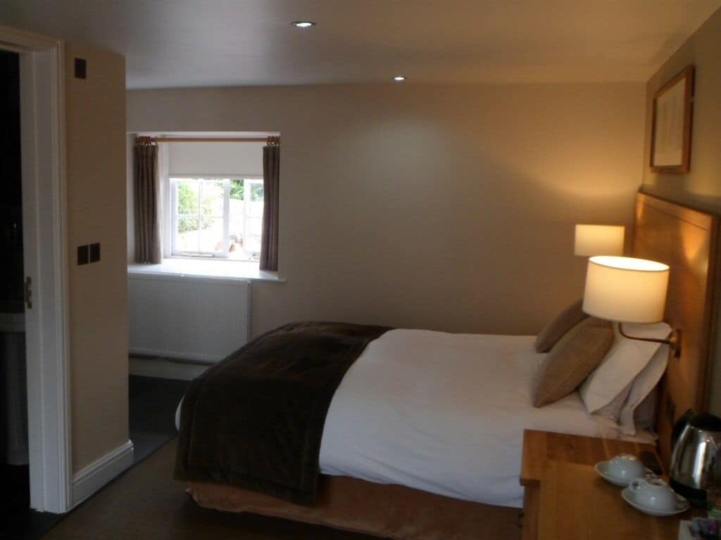 A bedroom with a bed, bedside table with a lamp, and a window with curtains.
