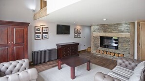 A living room with a stone fireplace, a television mounted on the wall, and a large wooden cabinet. - The New Inn (Dorchester)