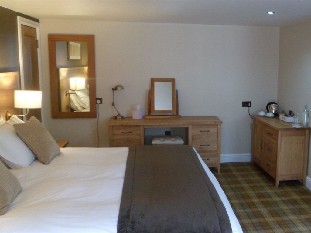 A hotel room with a bed, a desk with a mirror, a dresser, and a lamp.