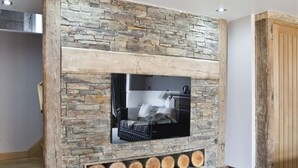 A modern living room with a stone fireplace, a flat-screen TV, and a wooden bench. - The New Inn (Dorchester)