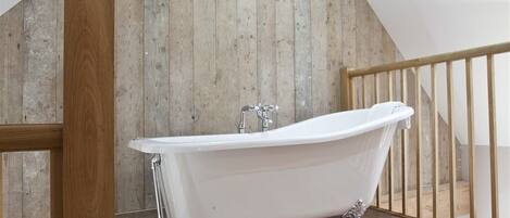 A freestanding bathtub in a room with wooden walls and a wooden floor.