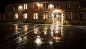 A stone building with a central entrance and multiple windows, illuminated by exterior lights. - The New Inn (Dorchester)
