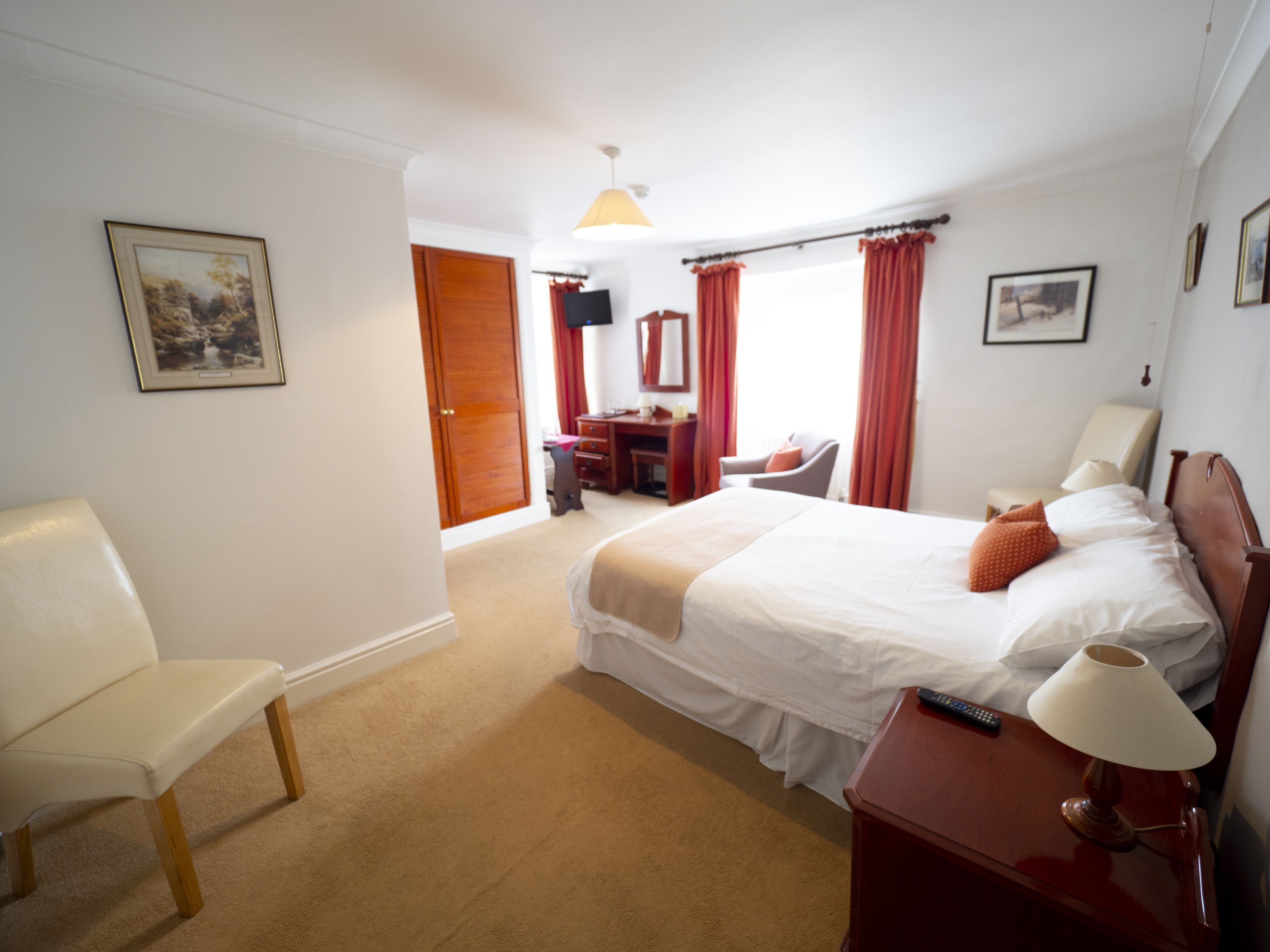 Habitación de hotel con cama, escritorio, silla, lámpara y televisor.
