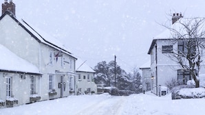 Une rue enneigée bordée de maisons blanches traditionnelles, avec une cheminée bien visible et une enseigne indiquant «
Hôtel Exmoor
».
