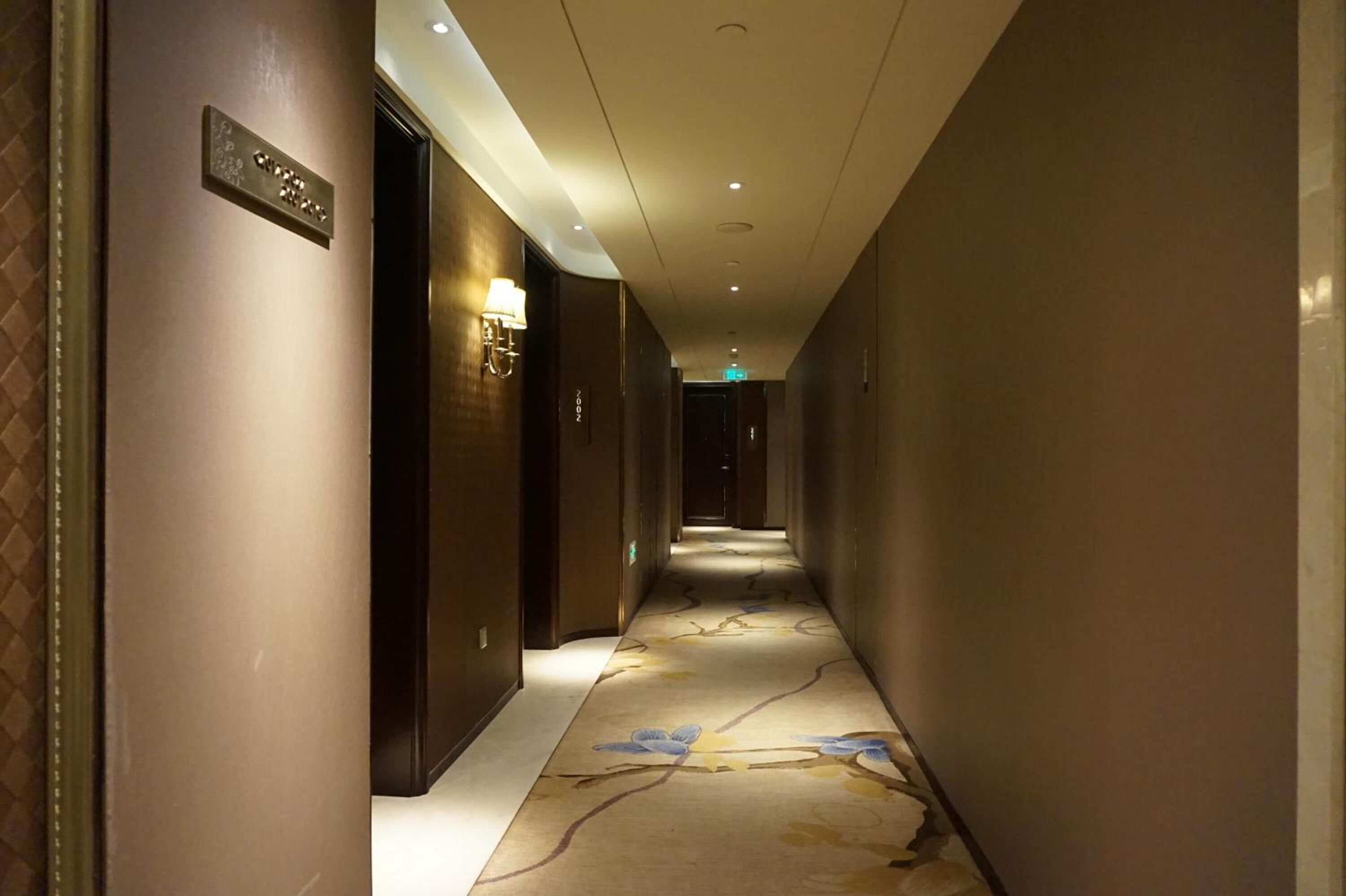 A hotel hallway with a carpeted floor, a sign on the left wall, and a door on the right.