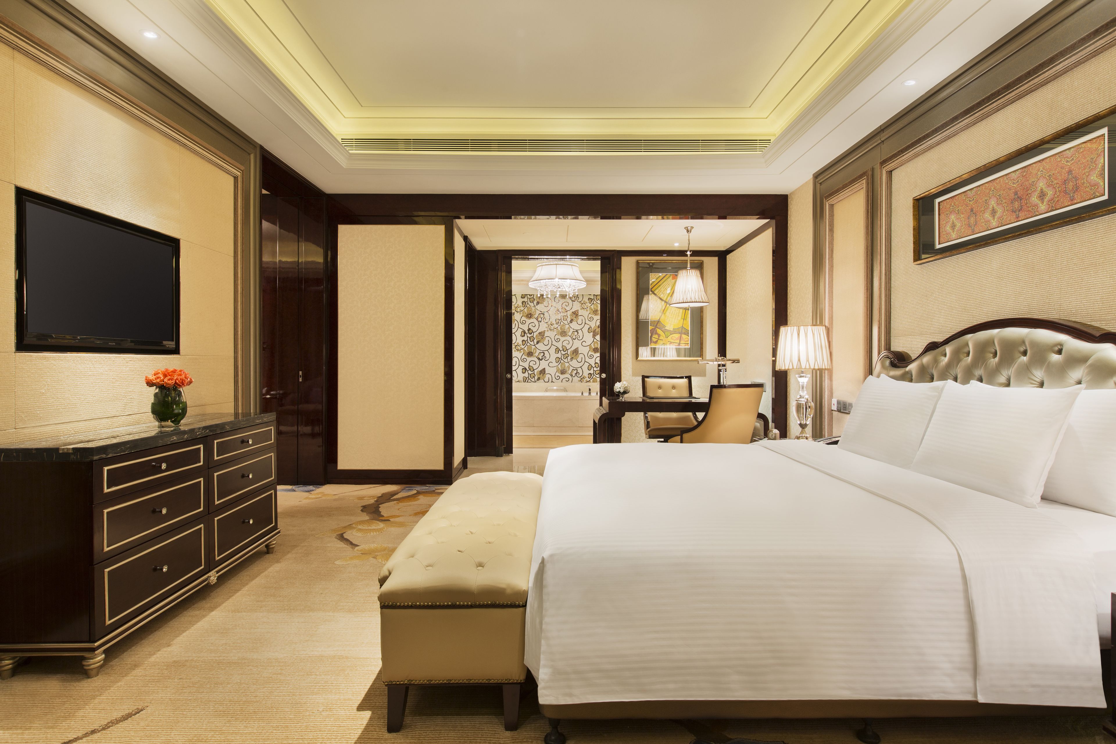 A hotel room with a large bed, a desk, a chair, a television, and a bathroom visible through an open door.