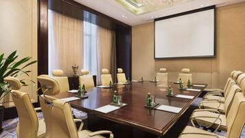 Un salón de conferencias con una larga mesa, múltiples sillas, una pantalla de proyector y un amplio ventanal con cortinas.