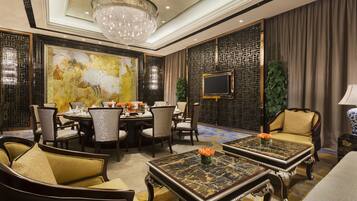 A luxurious hotel room with a dining area, two sofas, a coffee table, and a large painting on the wall.