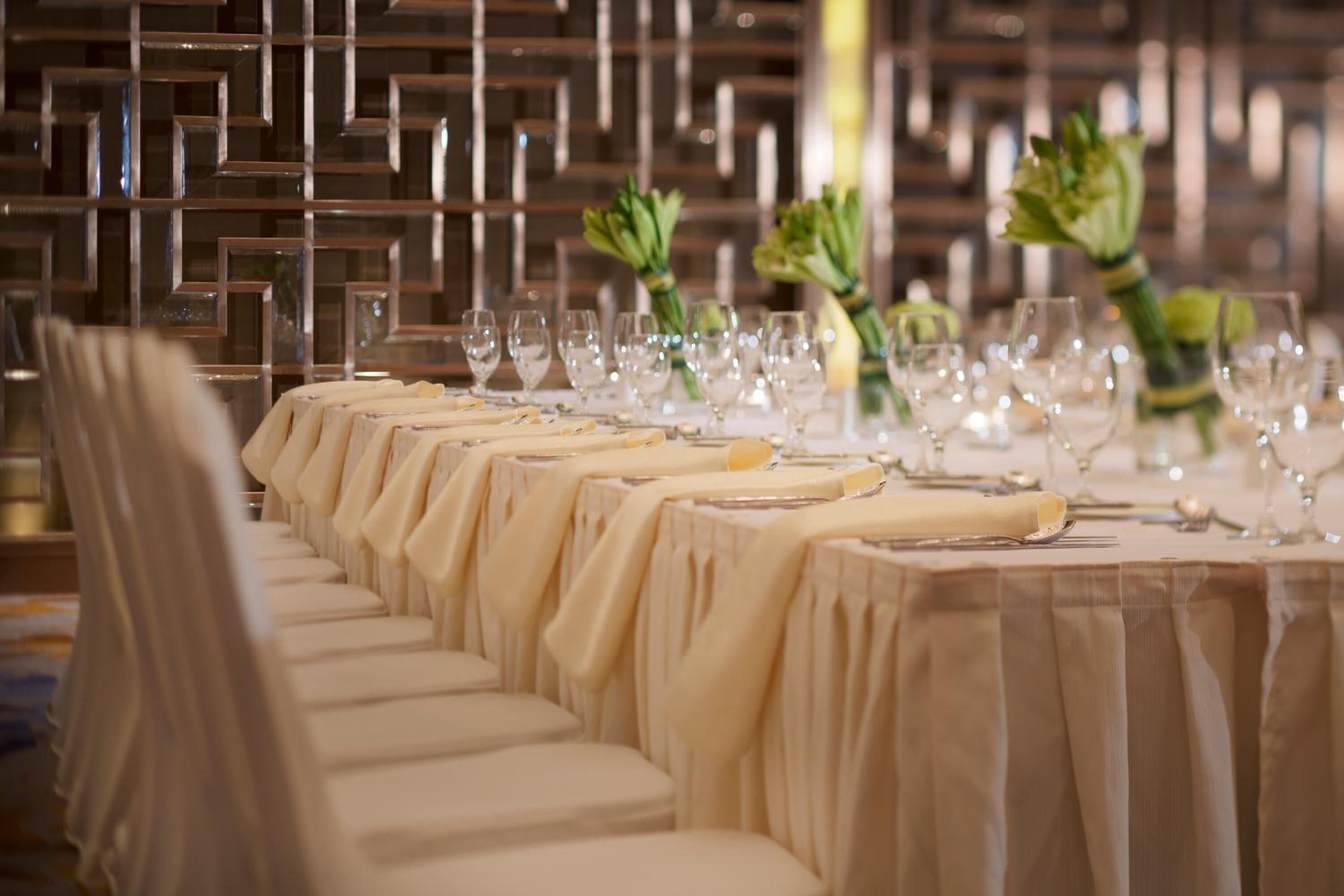 A long table set for a formal event with multiple wine glasses and a decorative centerpiece.