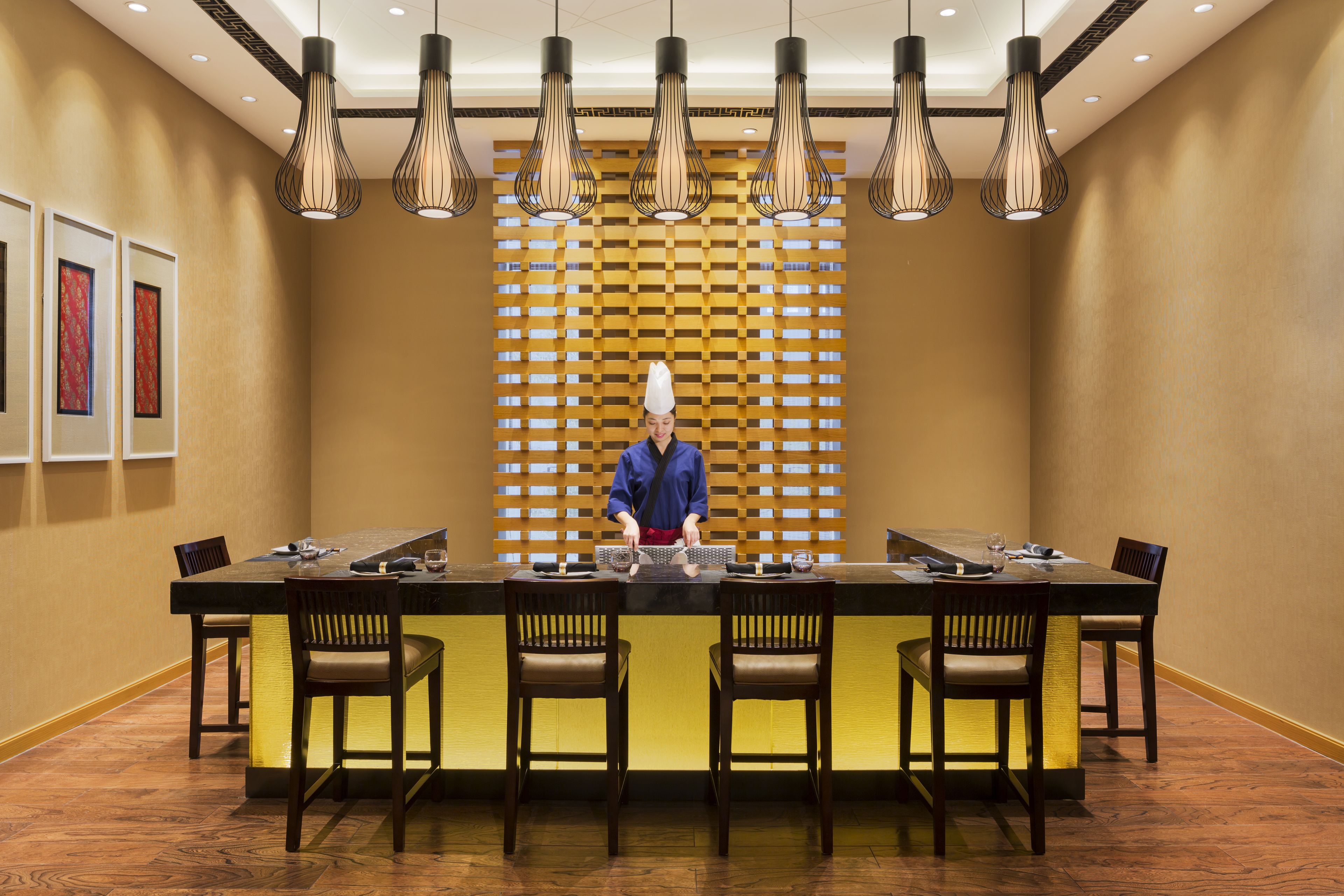 A restaurant with a long table, multiple chairs, and hanging pendant lights.