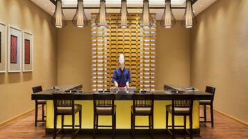 A restaurant with a long table, multiple chairs, and hanging pendant lights.